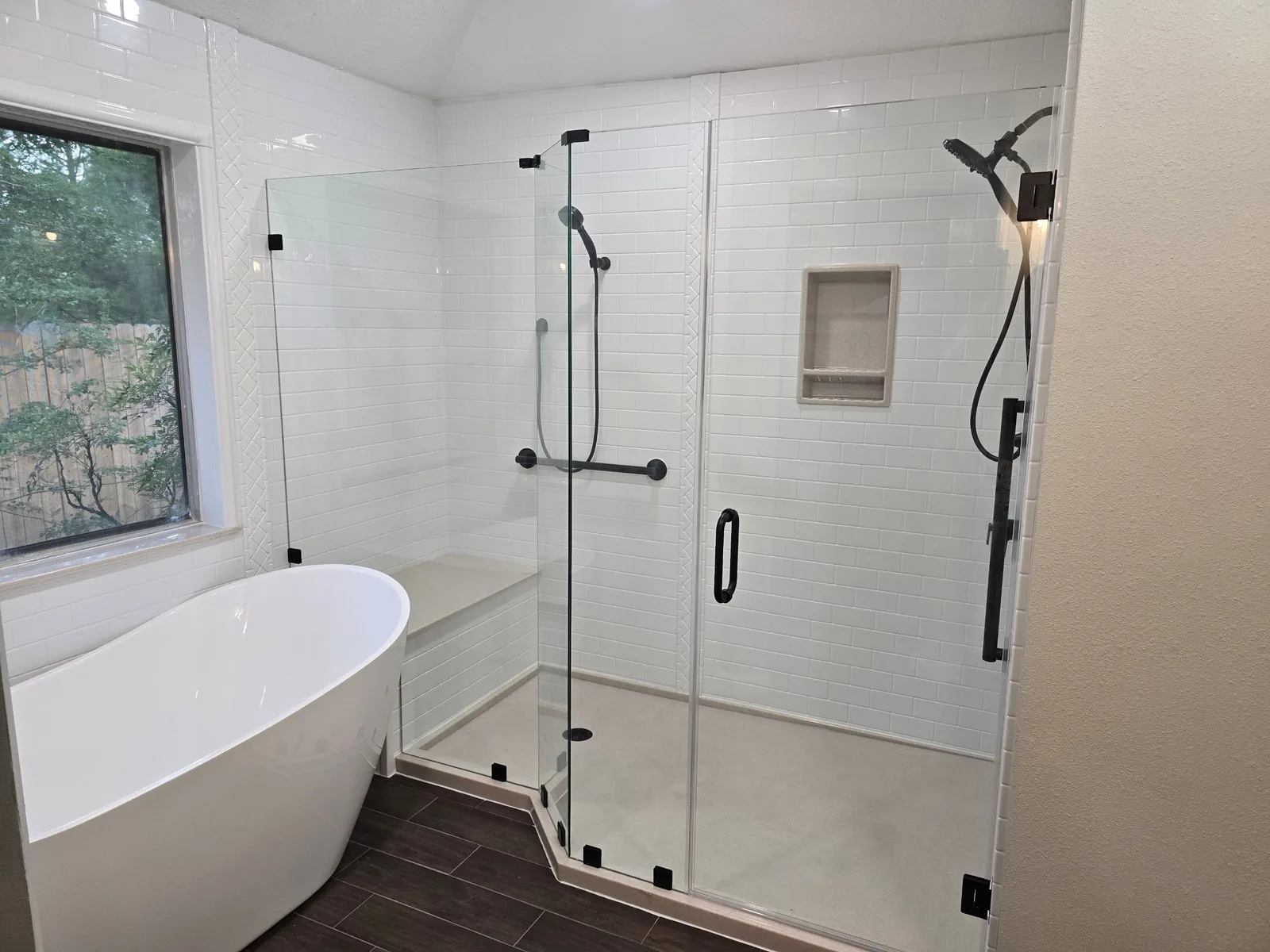 Houston remodel with white subway-pattern polymer walls, a custom-shaped Onyx shower base and bench, black hardware and freestanding tub