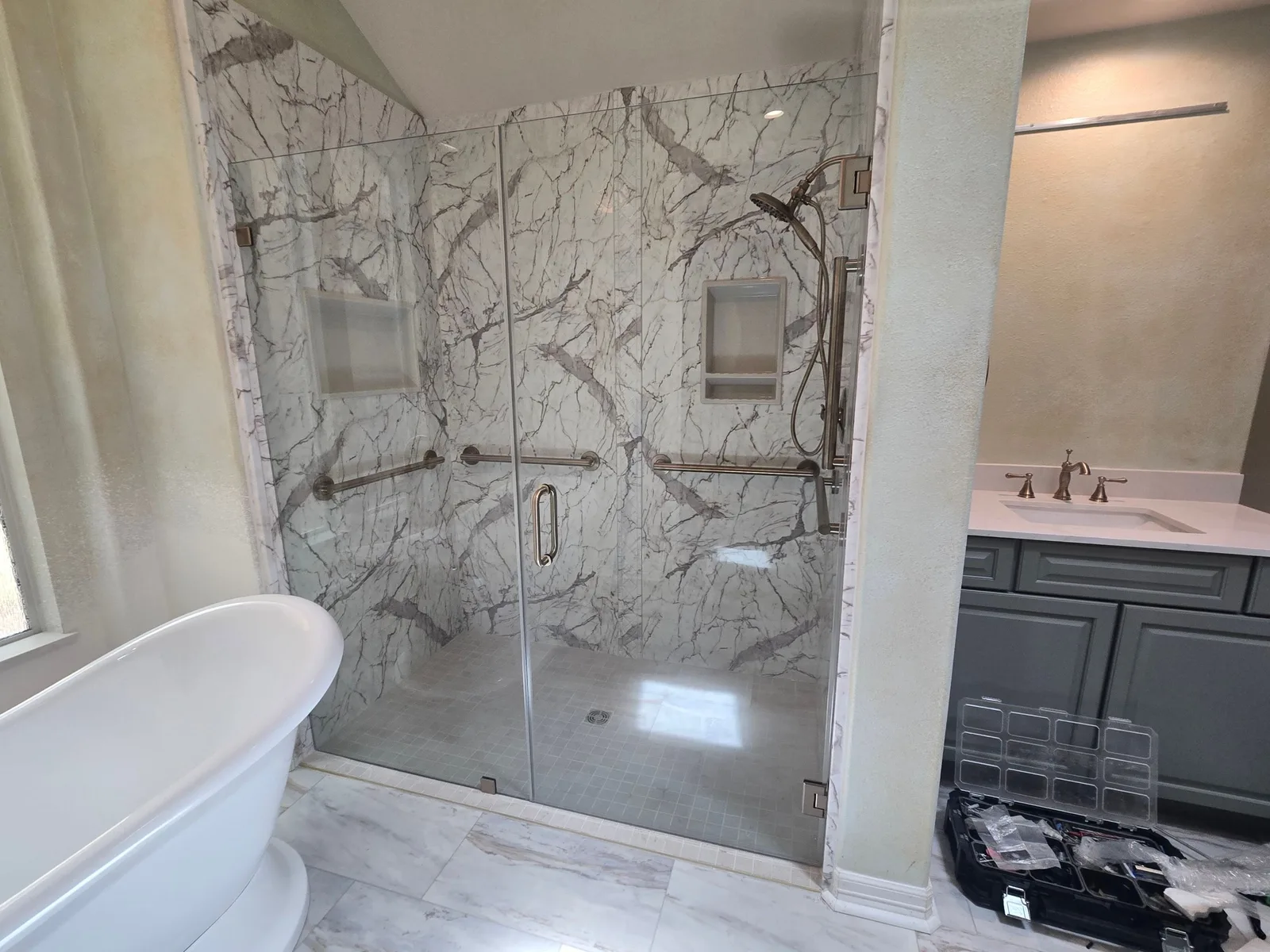 The Woodlands remodel with marble-pattern polymer shower walls, a tile shower floor, glass enclosure and freestanding tub