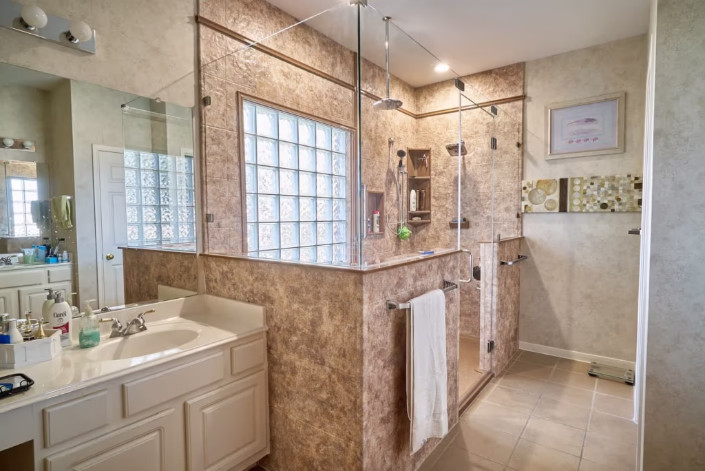 Corner shower with beige marble walls and glass block window