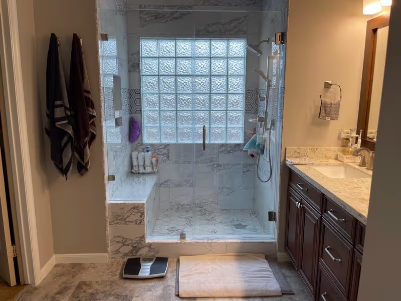 Modern bathroom with glass shower enclosure and large glass block window.