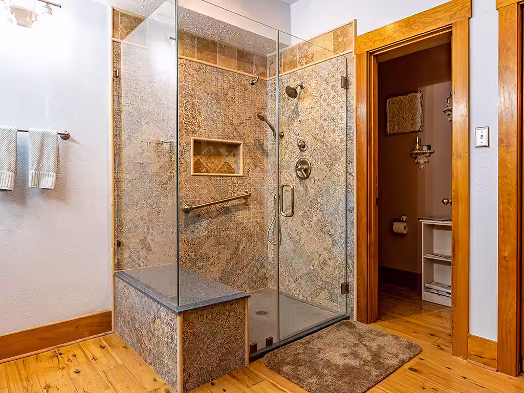 Custom shower remodel with textured mosaic tile, built-in bench and niche, frameless glass door, and bronze fixtures