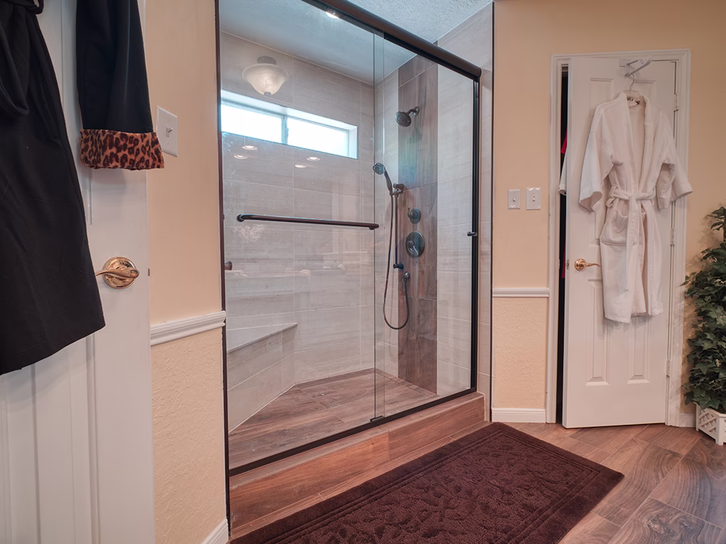 Tub-to-shower conversion with frameless glass enclosure, wood-look tile, built-in bench, and matte black fixtures