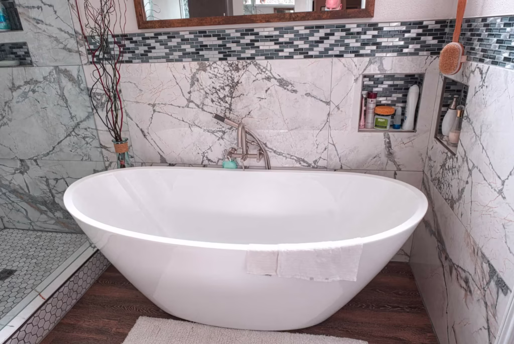 Freestanding white bathtub with marble tile accent wall