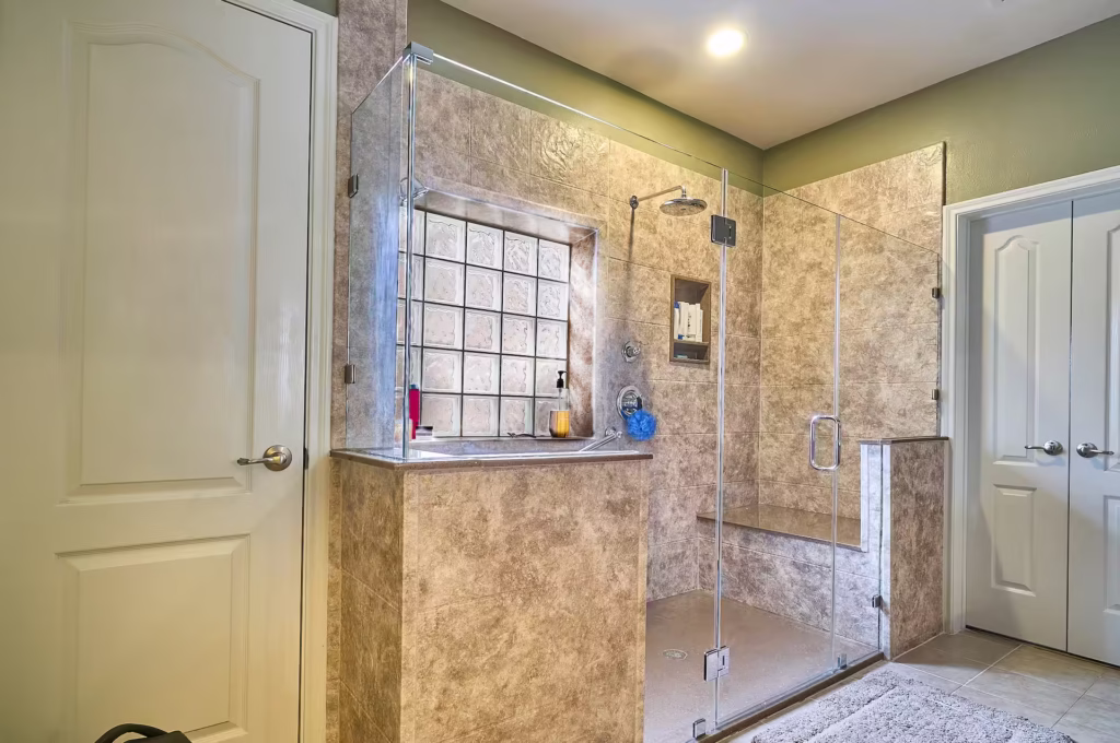 Walk-in shower with beige marble walls and glass block window