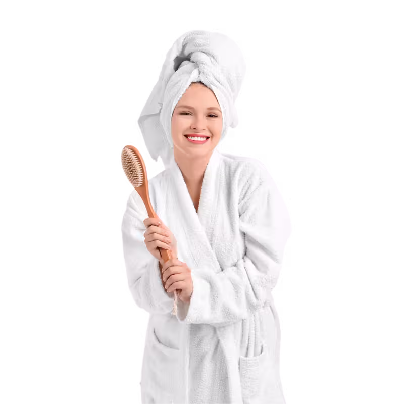 Smiling woman in bathrobe holding wooden bath brush
